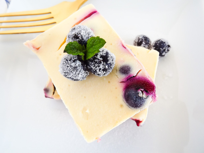 Close up of cheesecake bar on a plate with blueberries on top