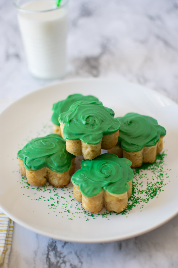 Five Baileys Cheesecake Stuffed Blondies on a plate with green sprinkles and a glass of milk in the background