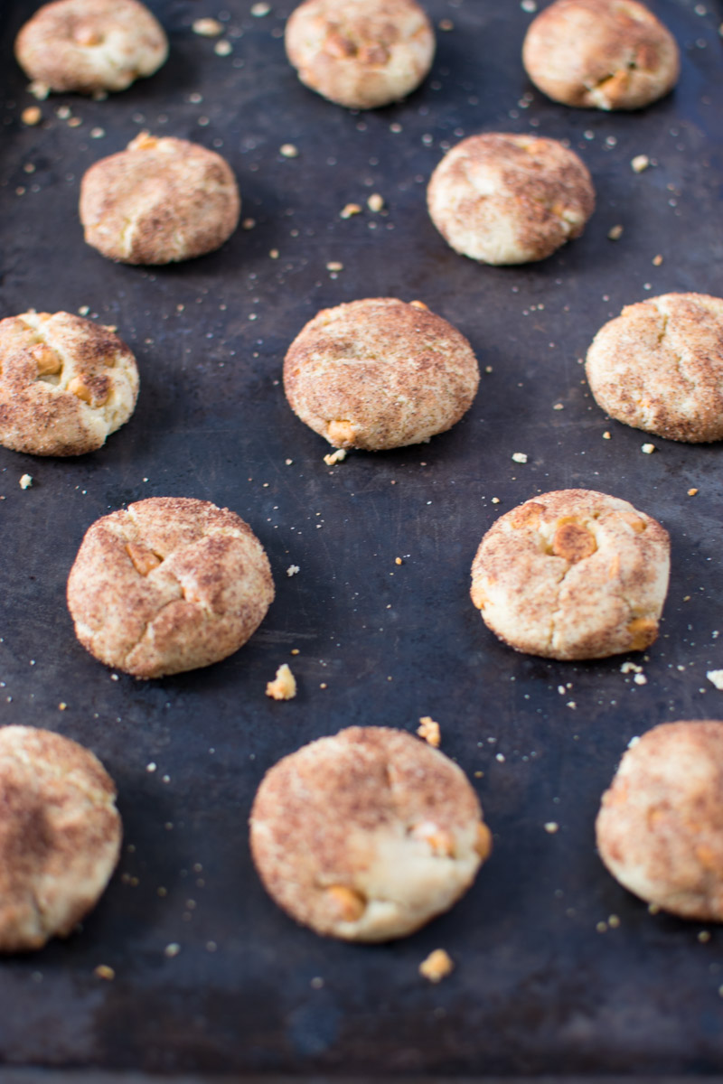 Lots of cookies on a dark baking sheet with cookie crumbs all over