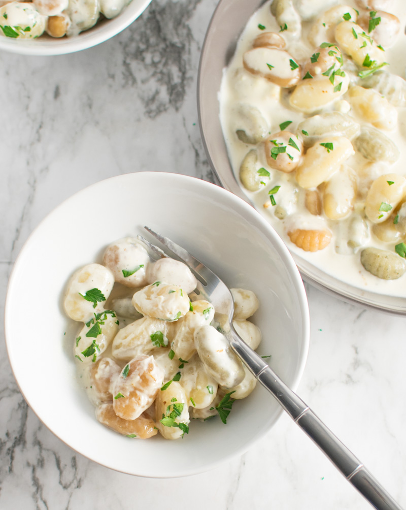 Overhead picture of Gnocchi with Gorgonzola Cream sauce in a small serving bowl with the corner of a large serving bowl