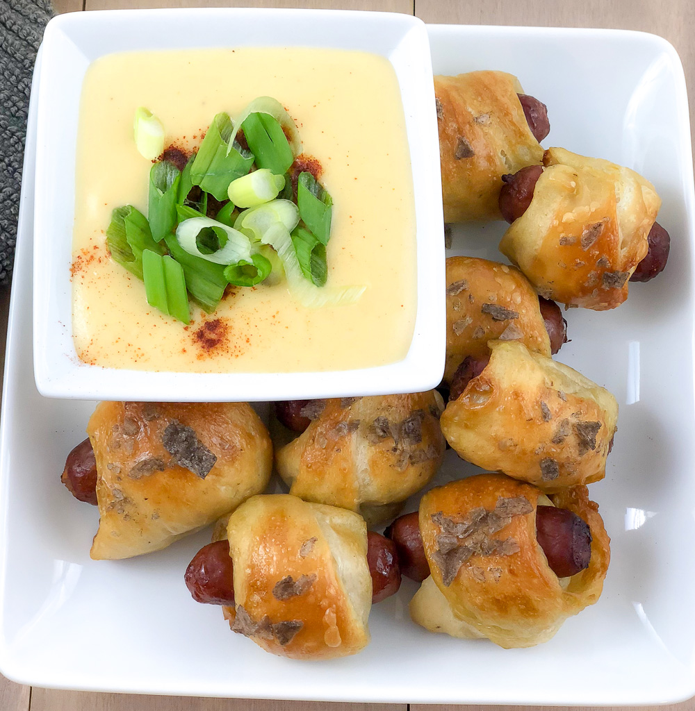 Close up picture of Pretzel Dogs on a plate with Beer Cheese Dip in a bowl topped with green onions