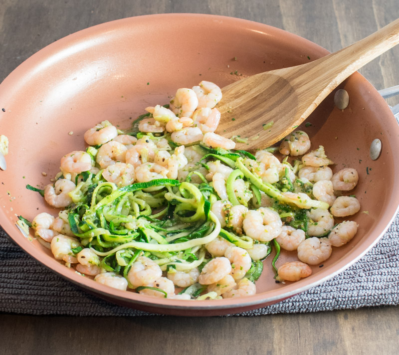 Adding pesto to shrimp and zoodles in a skillet