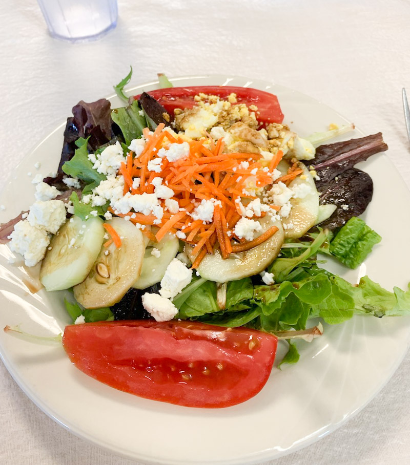 Salad from salad bar made with greens, cucumber, tomatoes, carrots, hard boiled egg, feta cheese and balsamic vinegar.