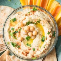 Overhead view of finished hummus in a bowl with pita chips and veggies