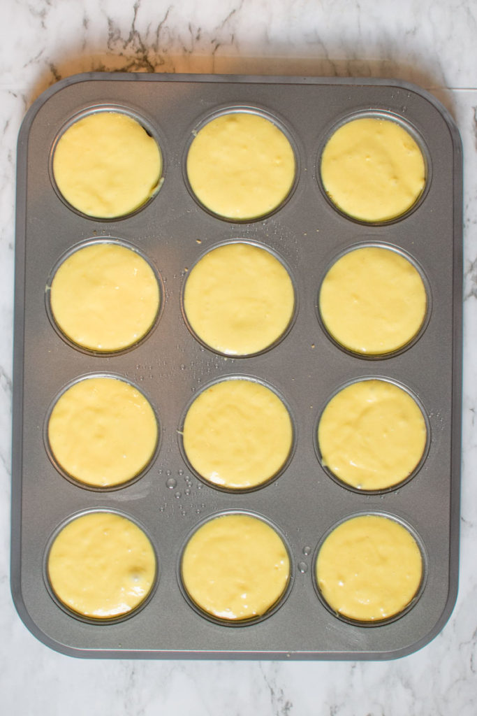 cupcake batter is spooned on top of crust in cupcake pan