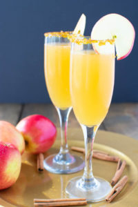 Two apple cider mimosas on a plate with apples and cinnamon sticks