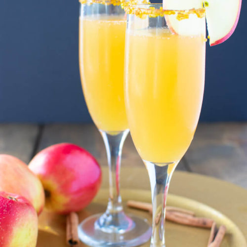 Two apple cider mimosas on a plate with apples and cinnamon sticks