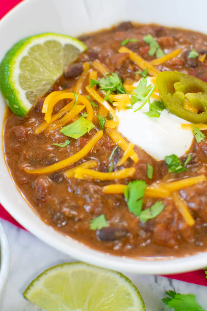 Closeup view of chili in white bowl with slices of lime