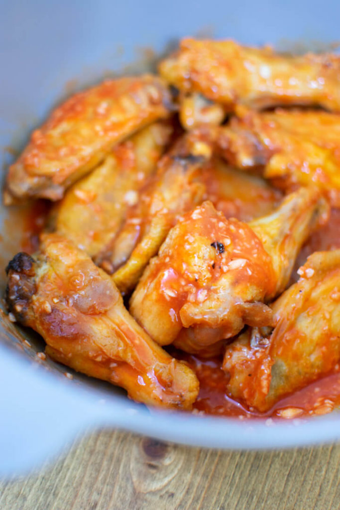 Cooked chicken wings mixed with hot sauce and garlic in bowl