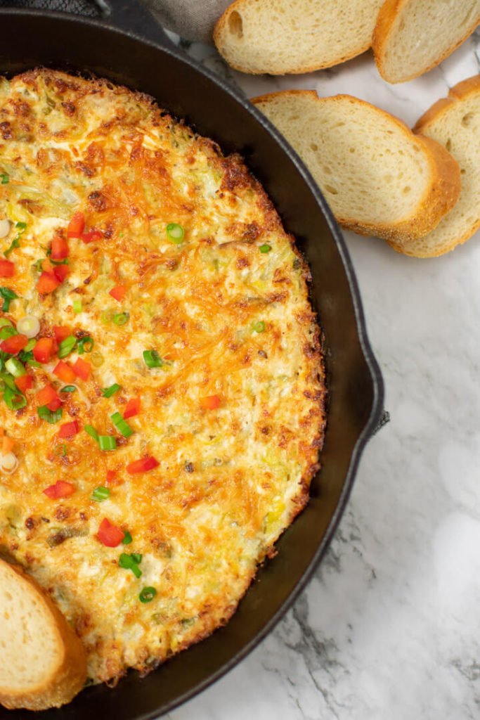 crab and artichoke dip in pan with baguette slices