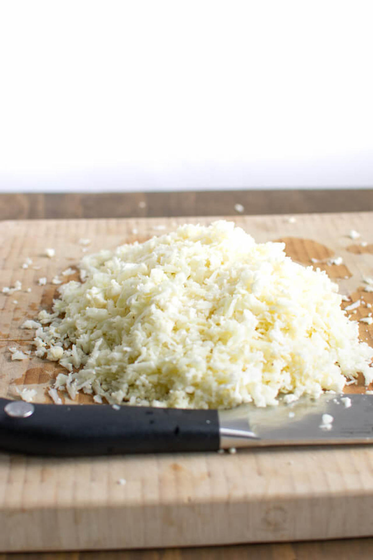 Pile of cauliflower rice on a cutting board made with the box grater
