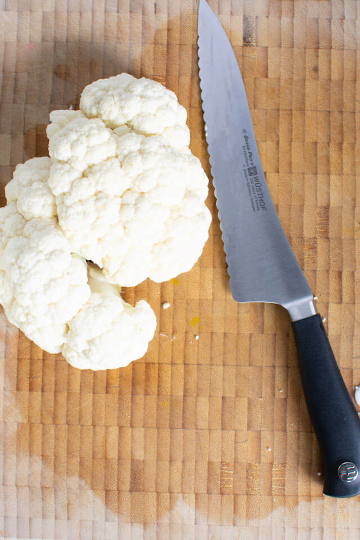 Cleaned and trimmed cauliflower on wooden cutting board with knife