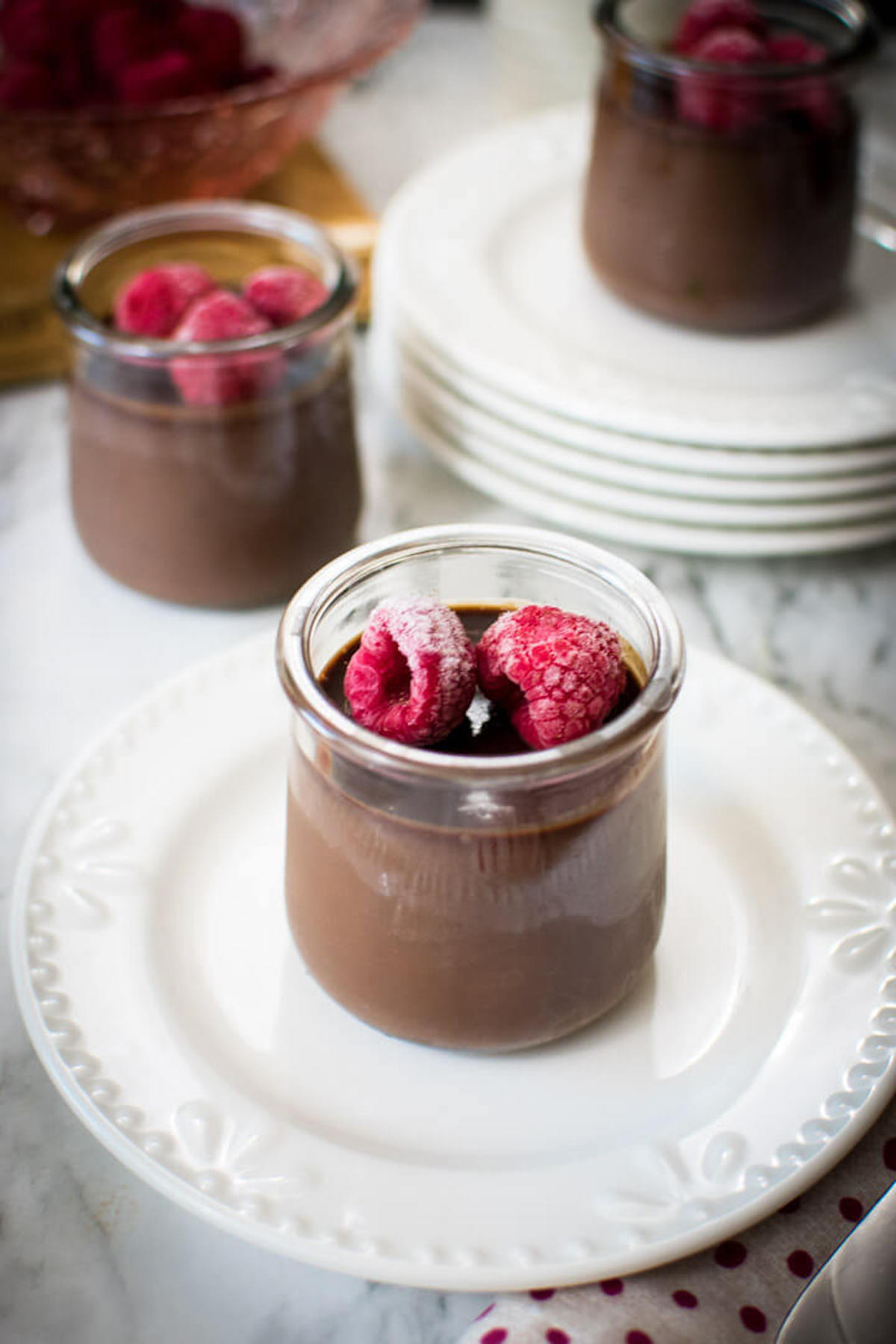 Closeup of a jar of chocolate custard with raspberries on top, jar is on a white plate