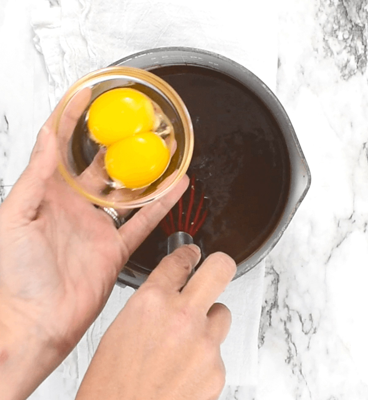 Adding egg yolks to chocolate in pan.