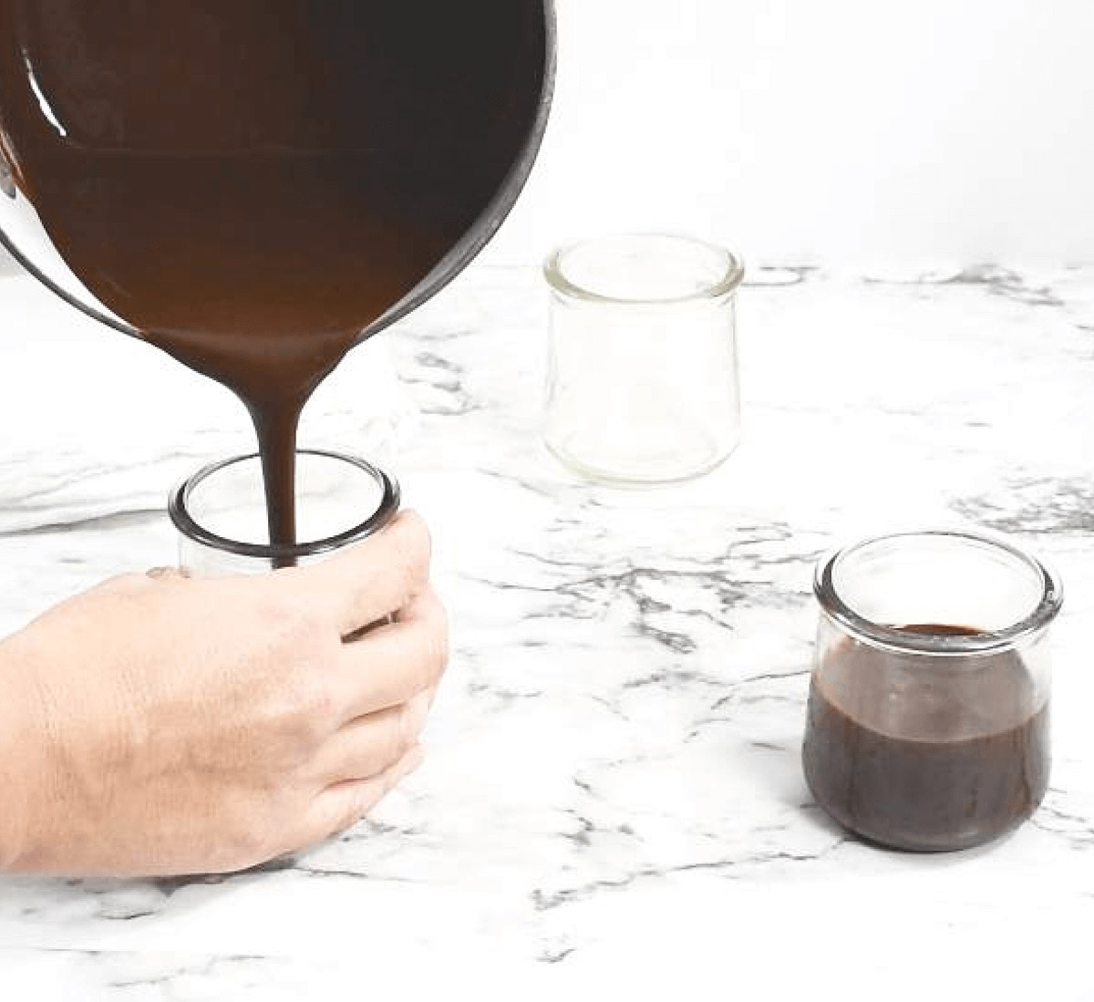 Pouring chocolate into small glass jars.