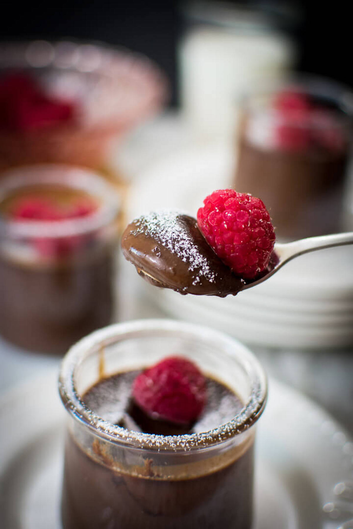 Closeup of a spoonful of chocolate dessert with a raspberry on top, sprinkled with powdered sugar.