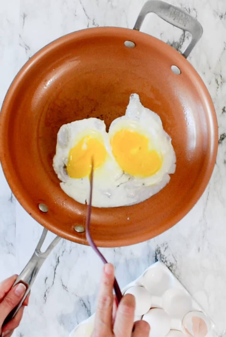 breaking the yolks of the eggs in the skillet with a spatula