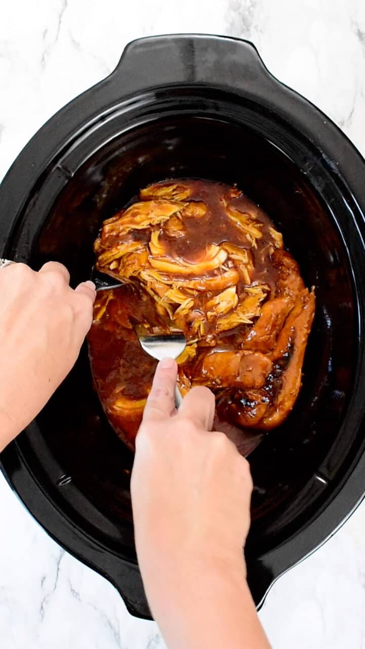 shredding chicken in slow cooker with two forks