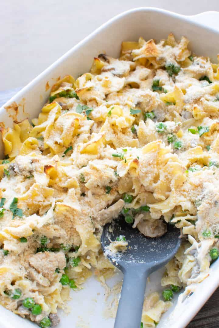 scooping chicken noodle casserole out of baking dish
