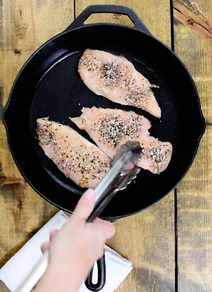 seasoned chicken breasts placed into a hot cast iron skillet with heated avocado oil
