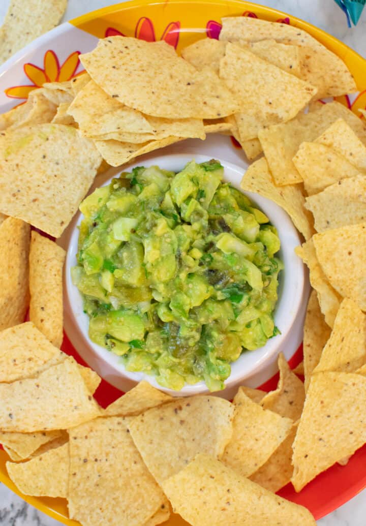 overhead view of easy roasted tomatillo avocado salsa with tortilla chips in bowl