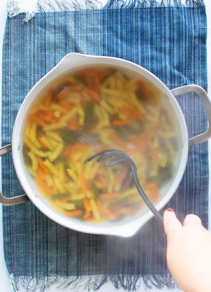 stirring tri color rotini pasta in a large pot of water