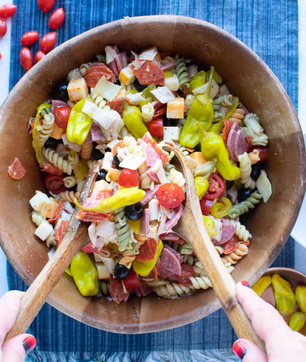 mixing all ingredients of pasta salad together in a large wooden bowl