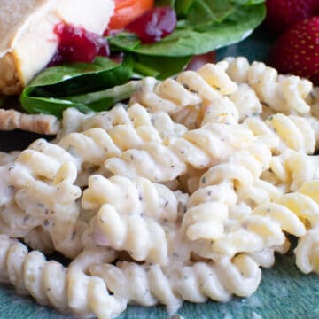 closeup of creamy pasta salad on plate with sandwich in background