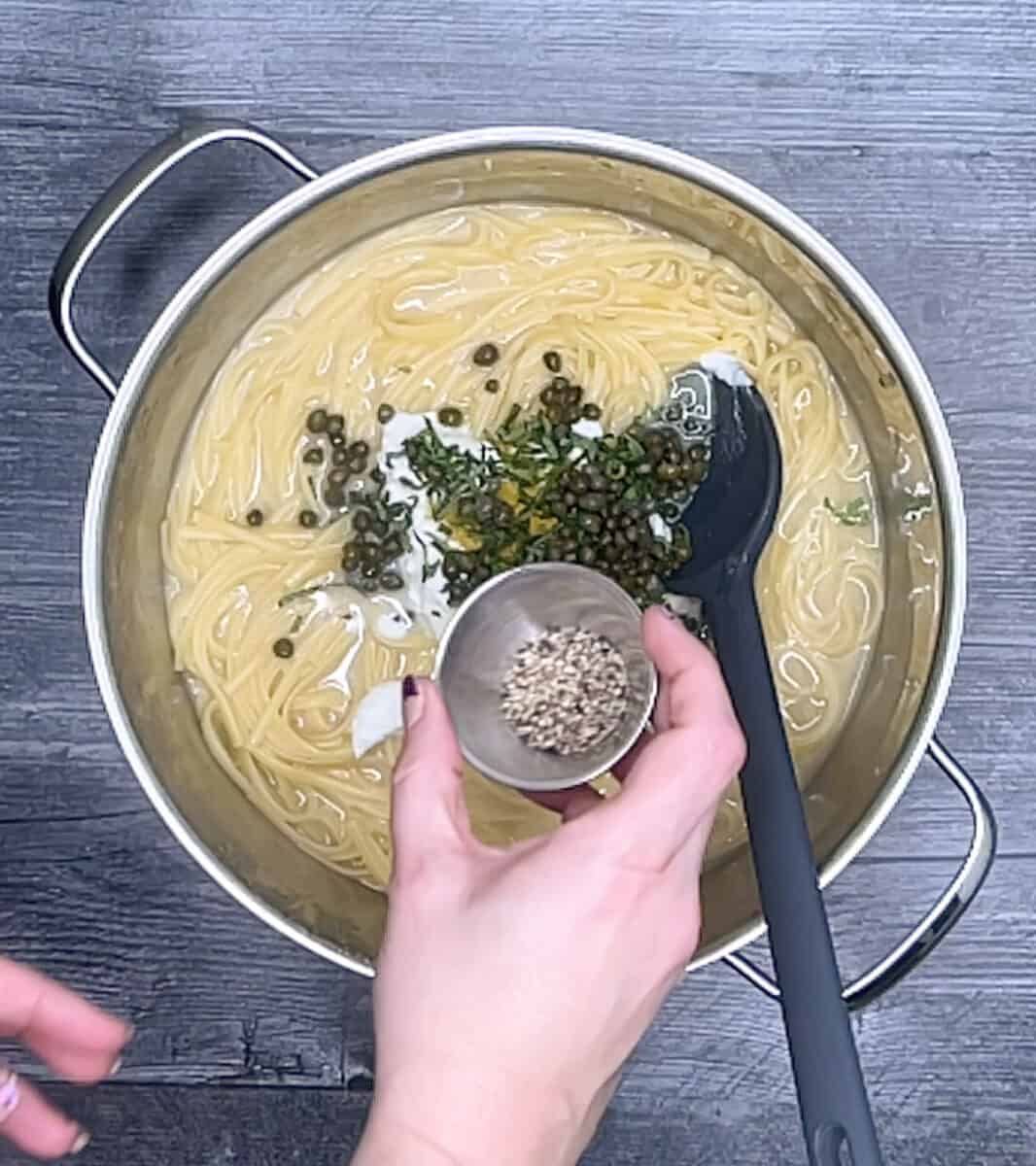 adding capers, basil and black pepper to pasta in pot