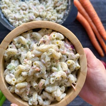 Hand holding a small bowl of deli Mac salad in a small wooden bowl