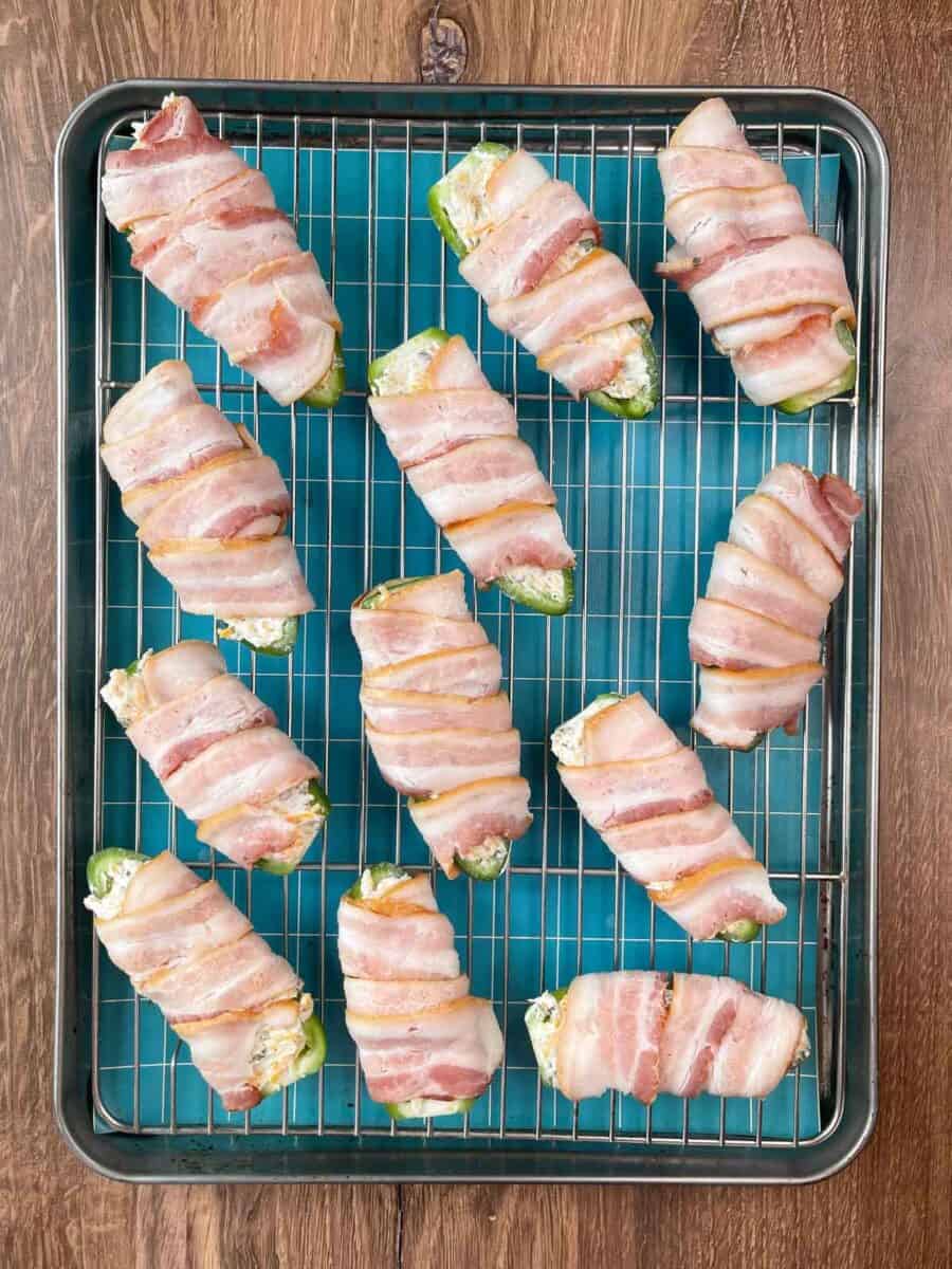 jalapeños stuffed with cheese wrapped in bacon on a baking tray with a rack ready for baking