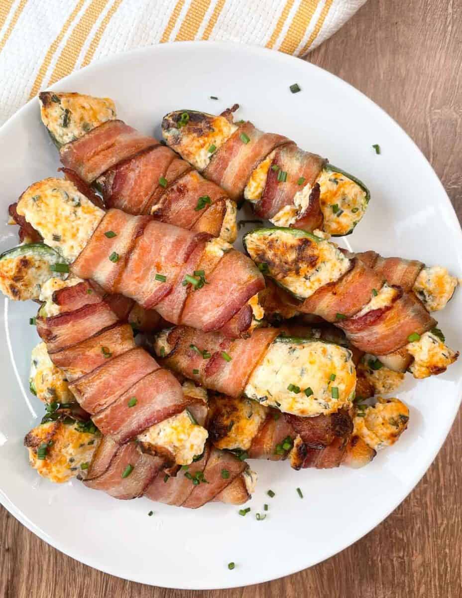 Bacon-wrapped stuffed jalapeños on a white plate with chives.