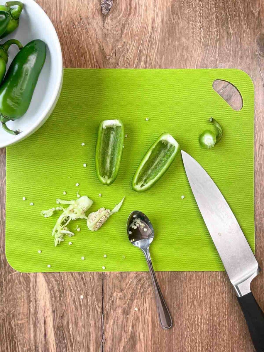 overhead view of removing seeds and membranes from jalapeño halves with a spoon