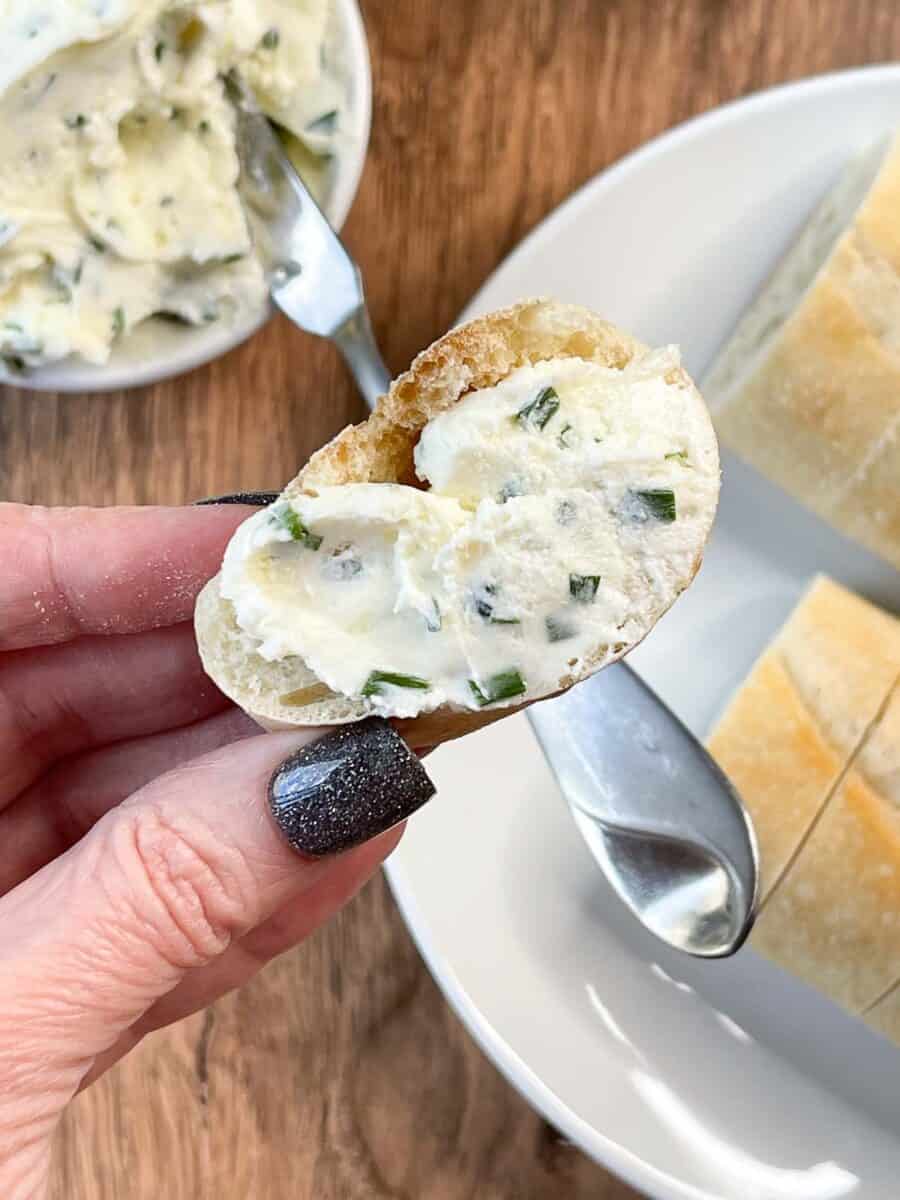 closeup view of one slice of baguette with garlic herb butter cream cheese spread on it