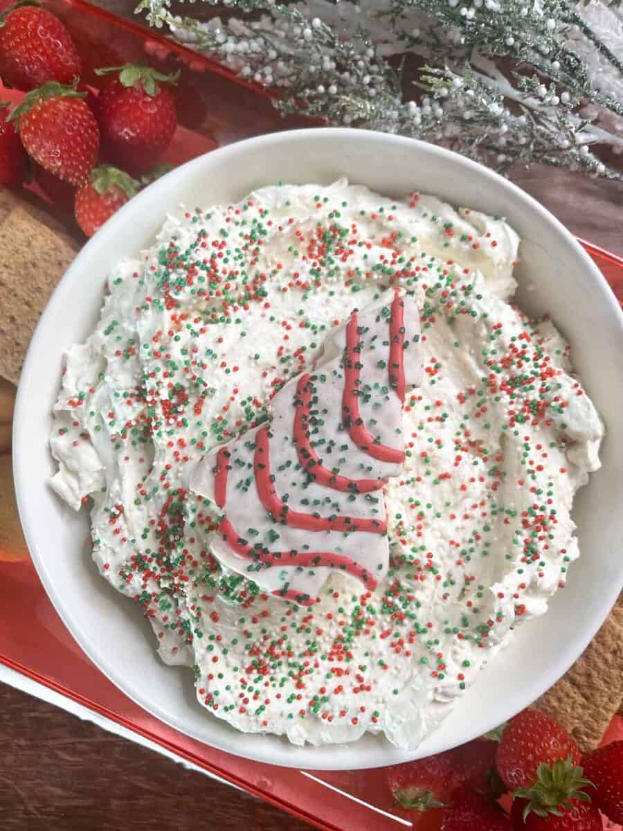 closeup overhead view of little Debbie christmas tree cake dip in a bowl with sprinkles on top and a whole tree cake on top