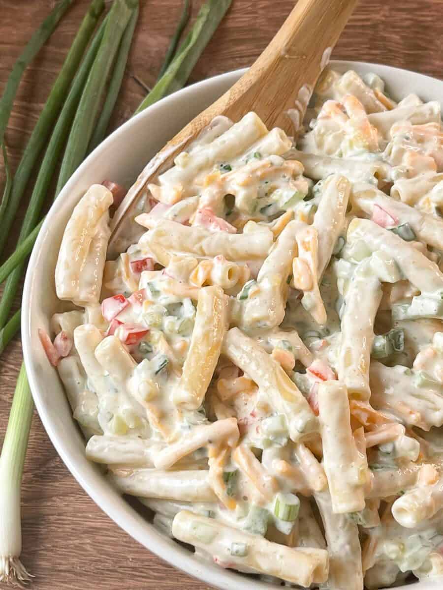 Closeup of cheddar and sour cream pasta salad in a bowl with green onions next to it