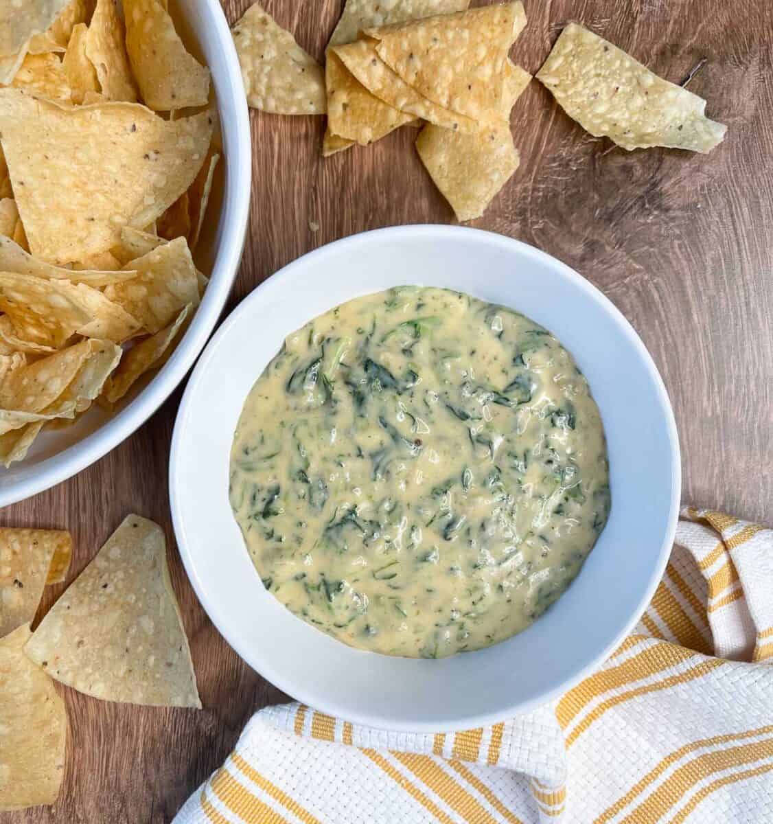 overhead view of spinach dip in a white bowl with a bowl of tortilla chips to the side
