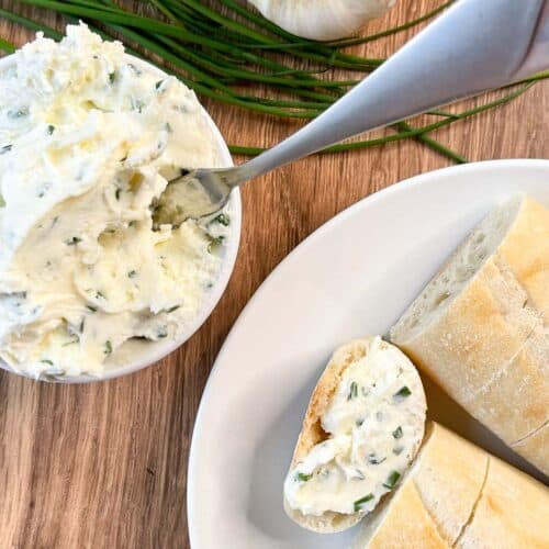 overhead view of garlic herb butter cream cheese spread in small bowl and a plate of bread with some spread on one piece