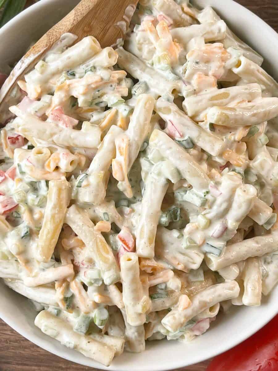 added sour cream cheddar macaroni salad to a serving bowl with a large wooden spoon