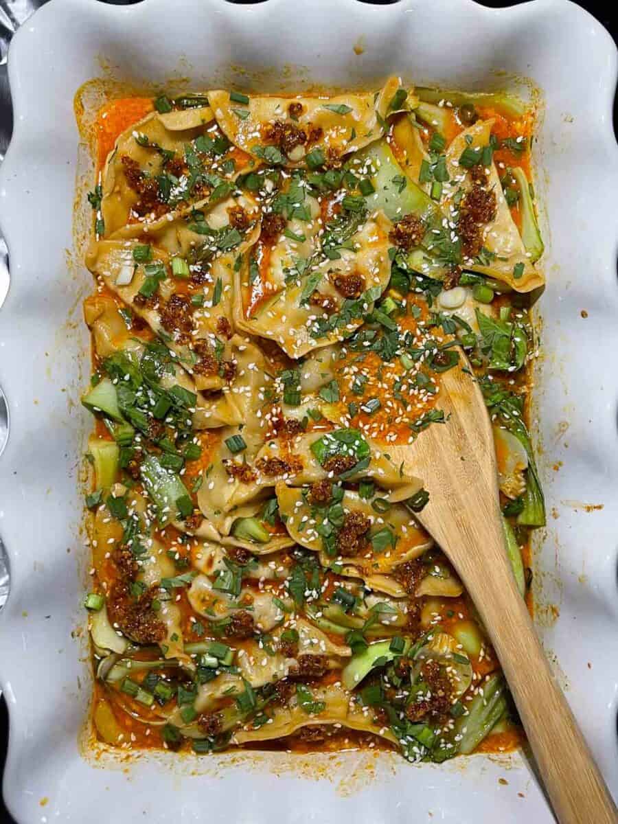 view of entire white dish with baked dumplings and bok choy with toppings added