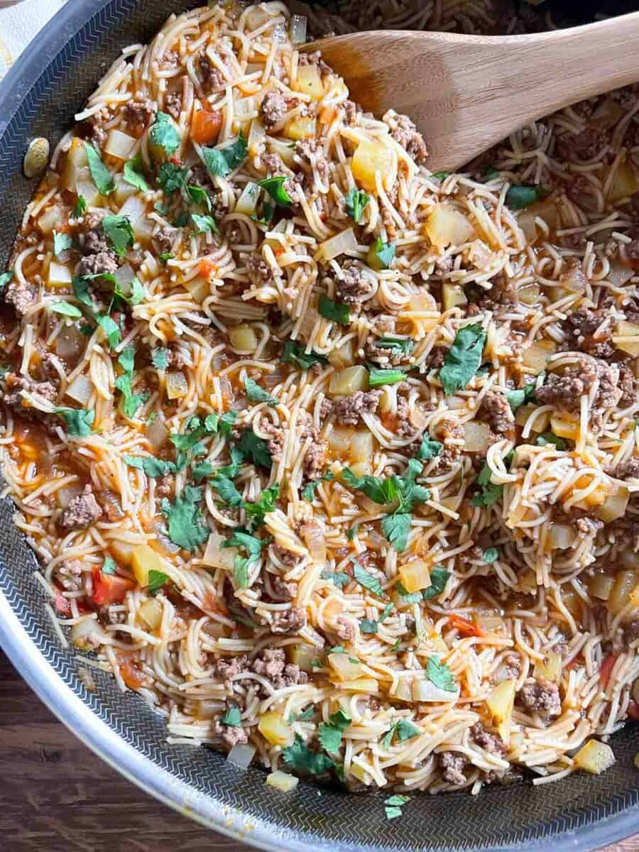 overhead view of finished fideo with ground beef in a skillet sprinkled with parsley and a wooden spoon in the pan