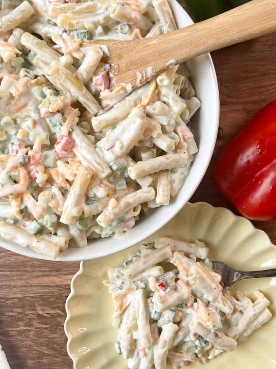 overhead view of cheddar and sour cream pasta salad in a white bowl and on a yellow scalloped plate