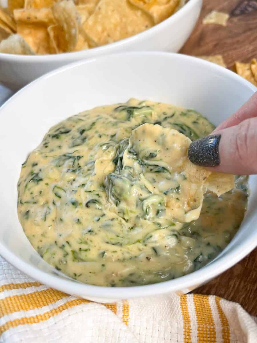 Close up of tortilla chip being dipped into spinach con queso.