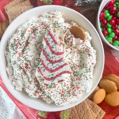 Close-up of holiday-themed whipped topping cake dip with colorful sprinkles on a festive table setting.