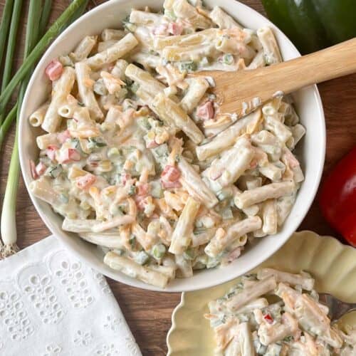 cheddar and sour cream macaroni salad in a white bowl with a wooden serving spoon and on a serving plate