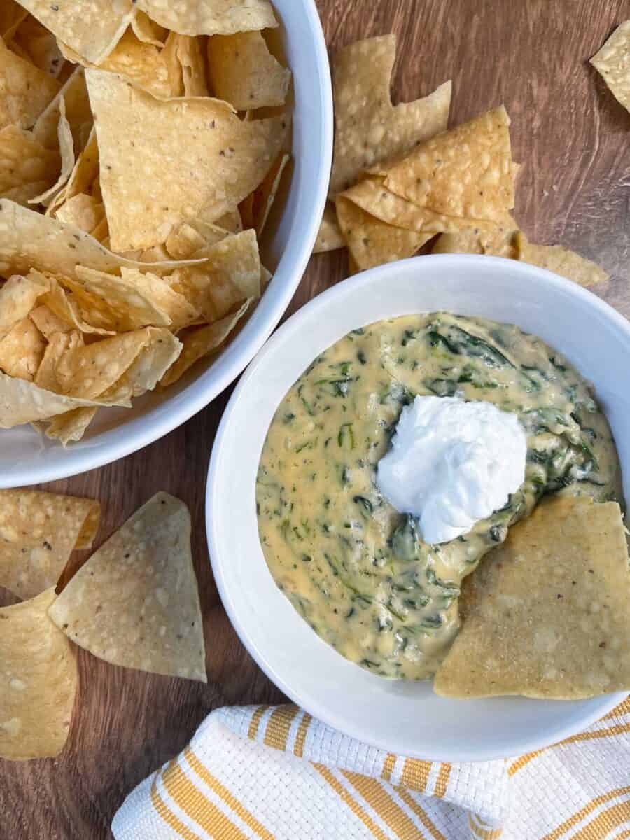 overhead view of spinach queso in a white bowl with a dollop of sour cream on top and a tortilla chip dipped in it