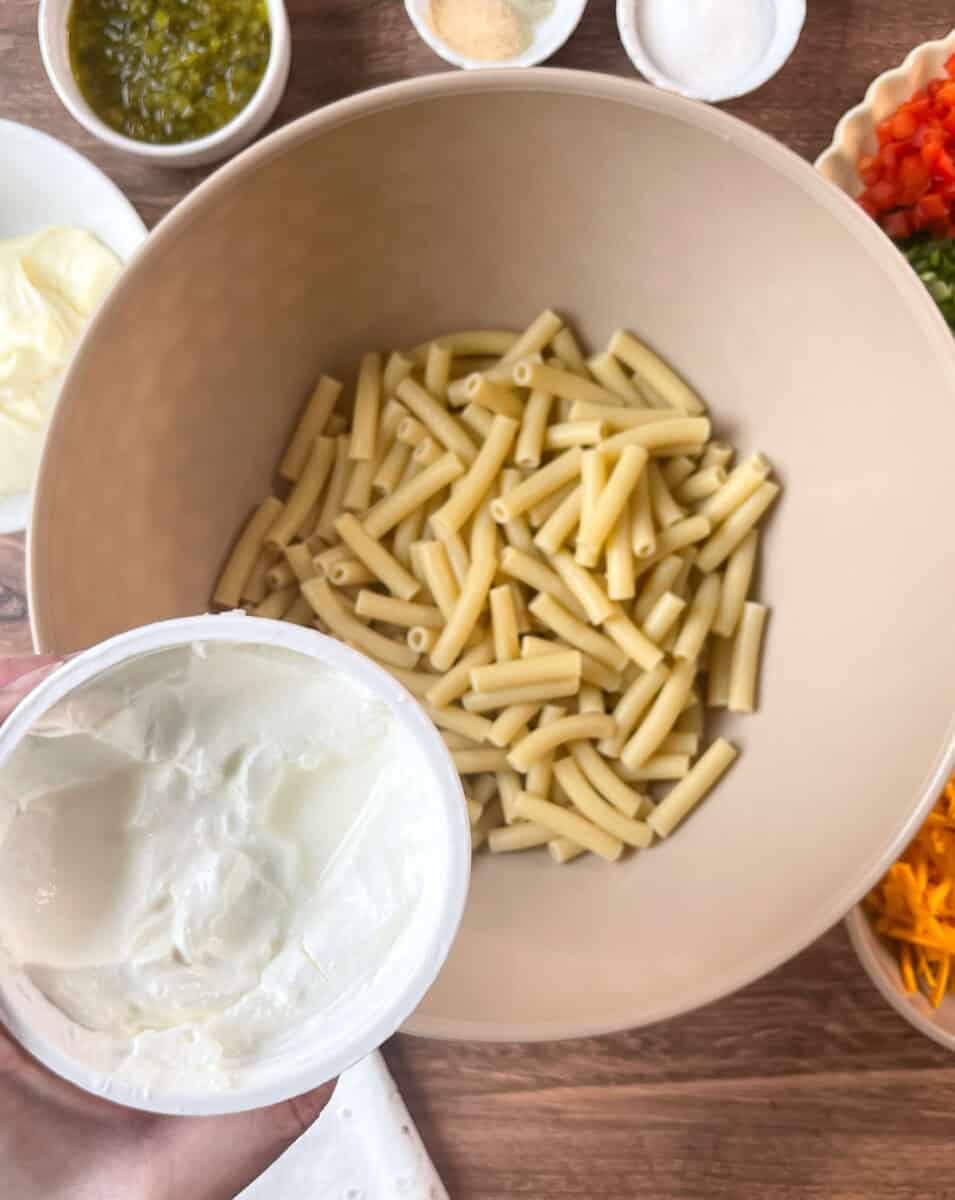 Adding sour cream to cooked macaroni in bowl