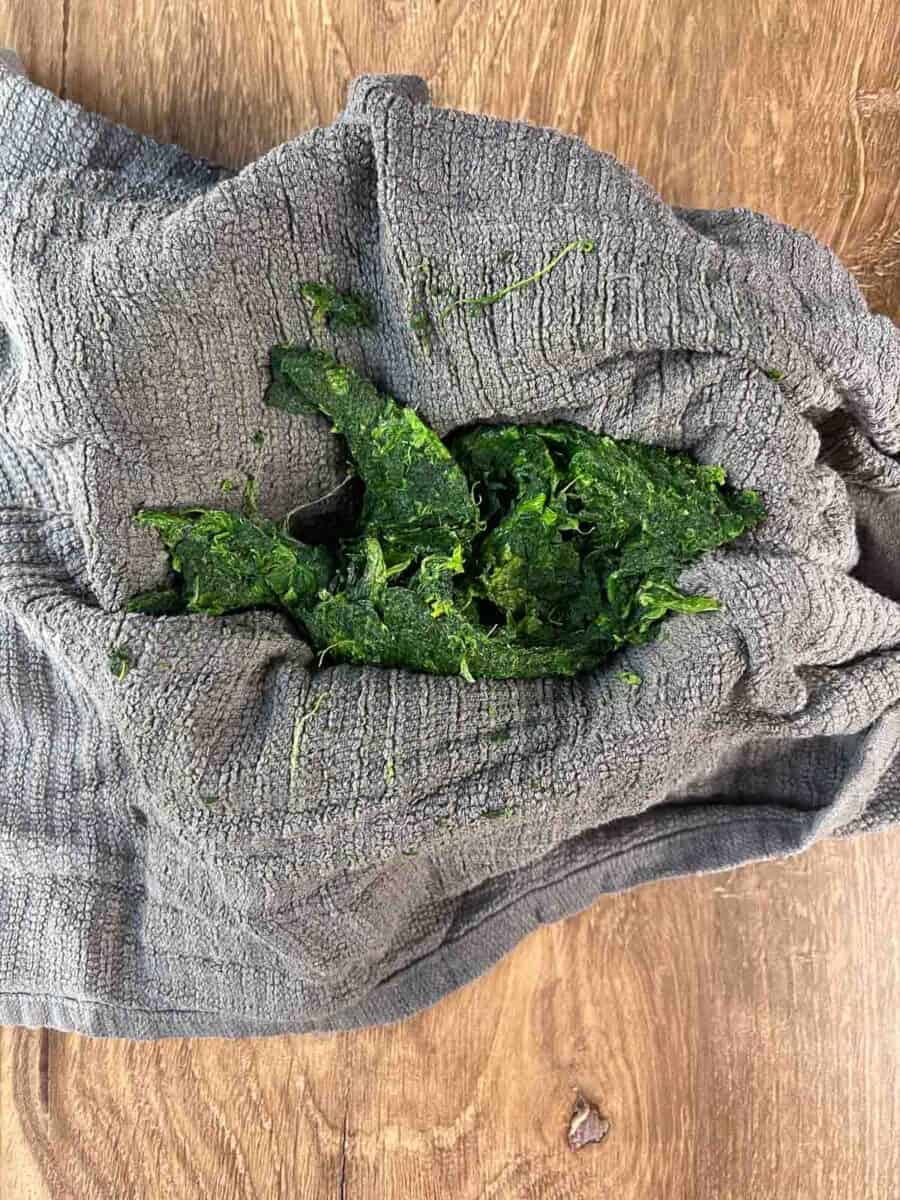 squeezing water out of thawed frozen spinach with a towel