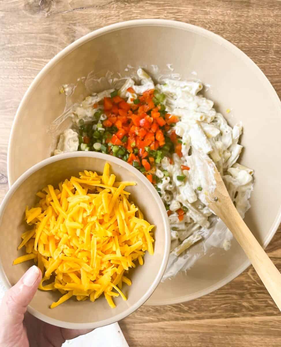 adding cheddar cheese to pasta in bowl