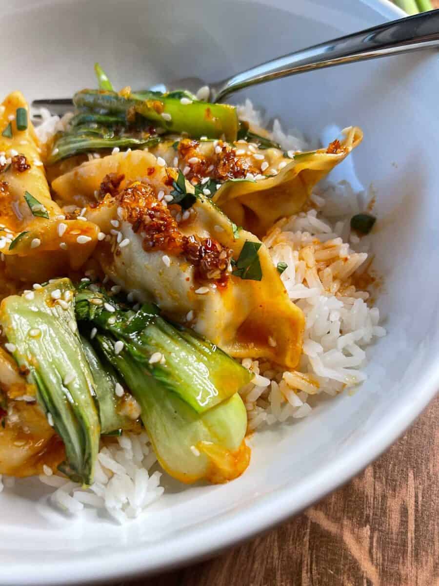 closeup view of baked dumplings and bok choy over rice in a white bowl